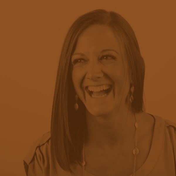 A woman smiling for the camera in front of an orange background.
